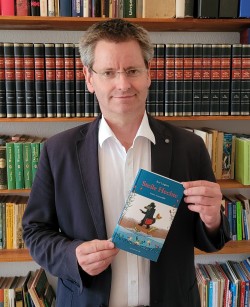 Bert Lingnau mit Buch vor Bücherregal