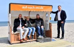 Matthias Fromm, Annette Rösler und Tino Ammon weihen den "Strandkorb für Alle" in Warnemünde am Strandaufgang 10 ein.