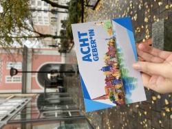 Postkarte "ACHTGEBER*IN" vor dem Rathaus.