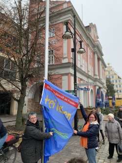 Ulrike Bartel und Dr. Cathleen Kiefert-Demuth hissen die Fahne mit der Aufschrift "Nein zu Gewalt an Frauen - Frei leben ohne Gewalt" vor dem Rathaus.