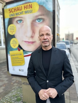 Senator Dr. Chris von Wrycz Rekowski vor dem Plakat "Schau hin und nicht weg!"