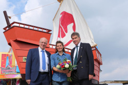 Im Rahmen der Auftaktpressekonferenz begrüßten Oberbürgermeister Roland Methling (li.) und Veranstaltungsleiter Holger Bellgardt Anne-Flore Gannat, die als Kapitänin der "Nordlys" das erste Teilnehmerschiff der 29. Hanse Sail im Rostocker Stadthafen festgemacht hat.