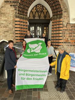 Hissen gemeinsam die Mayors of Peace Flagge: Oberbürgermeisterin Eva-Maria Kröger mit Vertreter*innen des Vereins IPPNV MV (Internationale Ärzt*innen für die Verhütung des Atomkrieges/Ärzt*innen in sozialer Verantwortung e.V.)